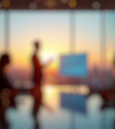 A silhouette of a person presenting in a conference room with a city skyline at sunset in the background.