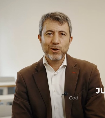 A man wearing a brown jacket is seated in front of a classroom, with 'JULIO RAMOS' captioned below him.