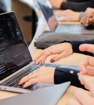 A person typing on a laptop with programming code displayed on the screen.