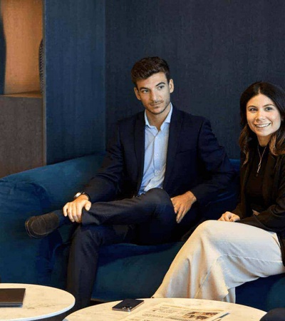 Four business professionals are sitting and engaging in a conversation in a modern office lounge.