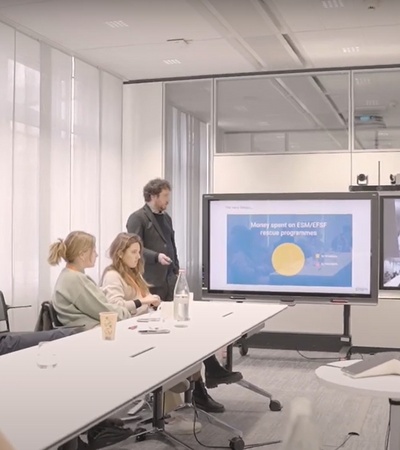 A group of professionals in a conference room watching a presentation on a large screen.