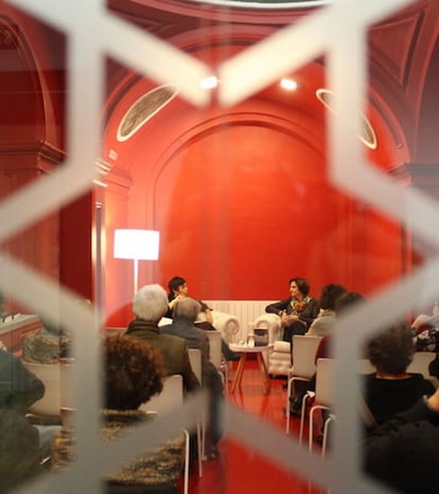 View through a decorative fence of a discussion panel inside a red room with attendees listening.