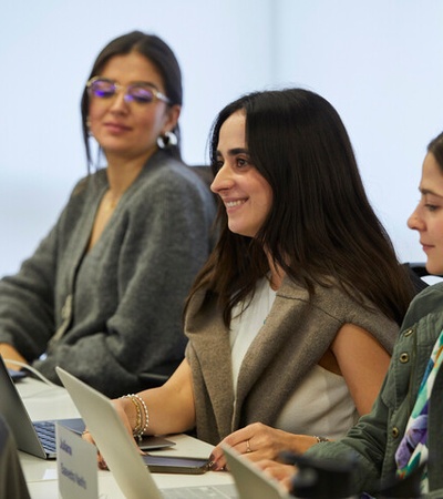 A group of three women smiling and engaged in a discussion in a modern workspace.