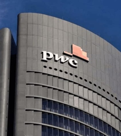 Modern curved office building with PwC logo against a clear blue sky.