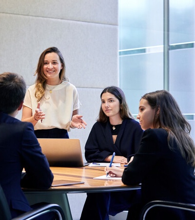 A business meeting with a woman presenting to three colleagues around a conference table.