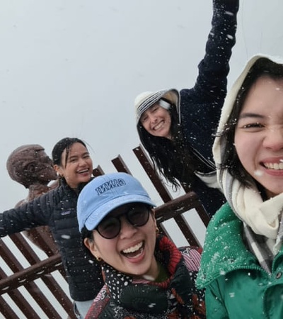 A group of four people, joyfully posing for a selfie in the snow with one person reaching her arm out to the camera.