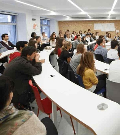A man is speaking to a group of attentive adult students in a modern classroom setting.