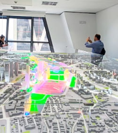 Group of people observing a colorful 3D city model display in a modern office setting.
