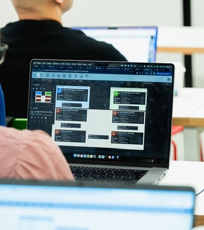 A group of people in a classroom setting, focusing on a laptop screen displaying various software applications.