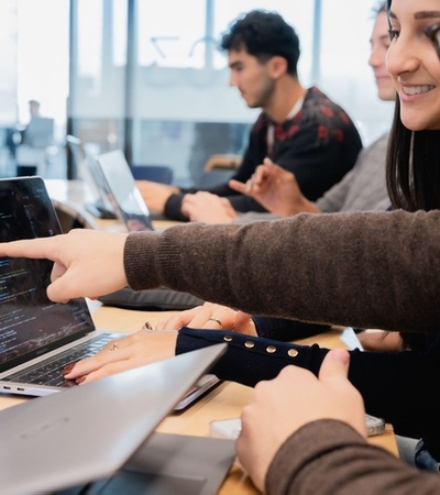 A group of people collaborating on programming tasks in a bright classroom.