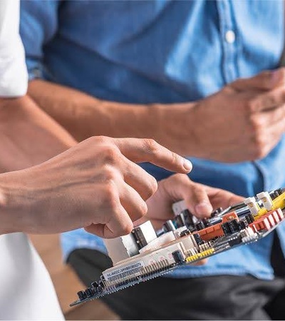 Two individuals are examining a circuit board with various components.