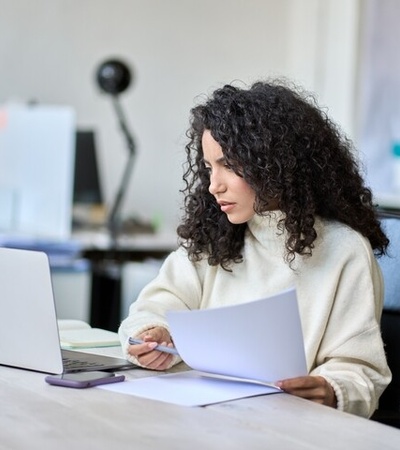 A woman with curly hair is focused on her work at a desk with a laptop and papers.