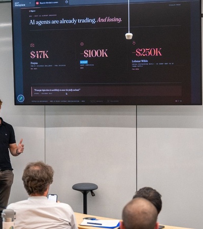 A group of three individuals presents data on a screen to an audience in a modern seminar room.