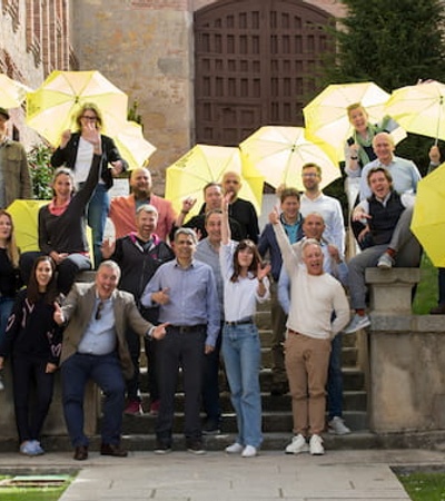 A group of people holding yellow umbrellas are posing on steps outside a building.