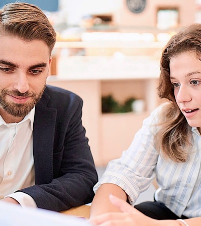 A man and a woman are discussing over a document in a bright office environment.
