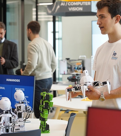 A young man demonstrates a robotic drone in a modern tech environment with various humanoid robots on display.