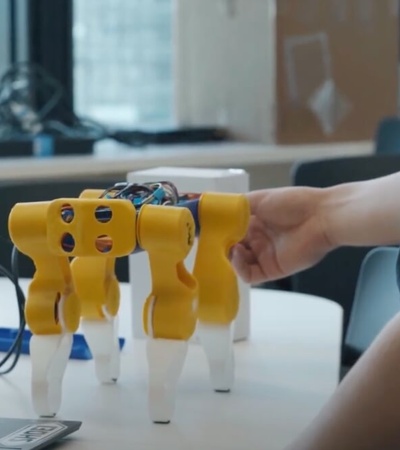 A person testing a small yellow robotic dog in a tech lab environment