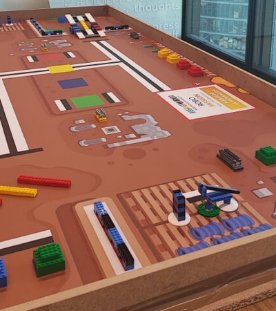 A large table displays a colorful urban planning model with various building blocks and street layouts.