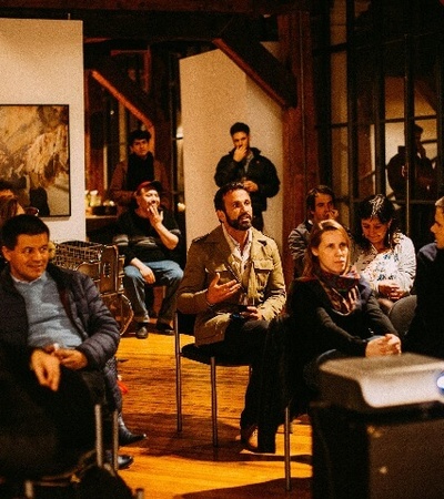 A group of people attending a presentation in a cozy room with wooden accents and dim lighting.