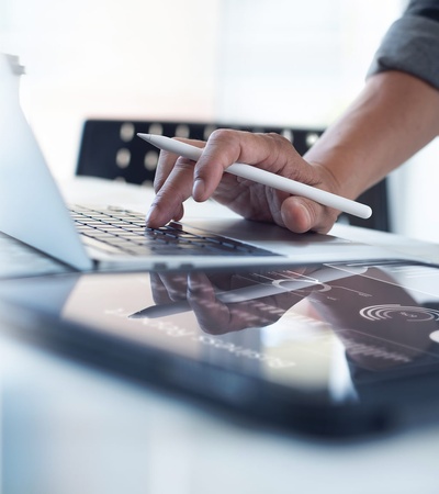 A person using a stylus on a tablet while typing on a laptop.