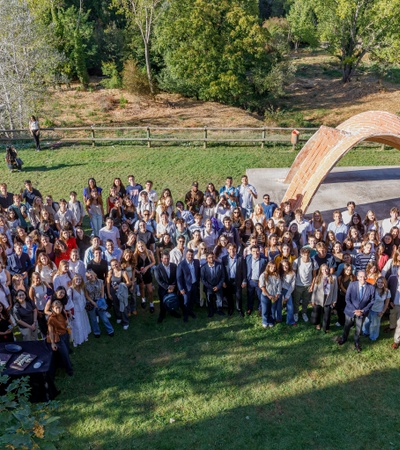 A large group of people gathered outdoors in front of an arch-shaped structure.