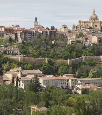 A panoramic view of a historic city with a prominent cathedral and surrounding walls set on a hill.