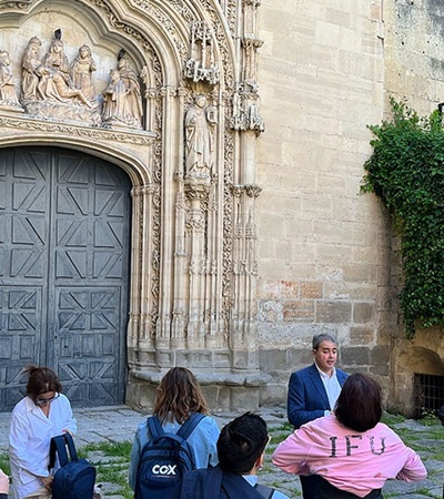 A tour guide is explaining history to a group of tourists in front of an ornate building.