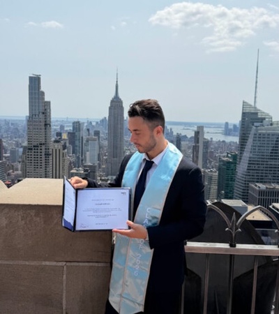 A man stands on a rooftop holding a certificate with a city skyline in the background.