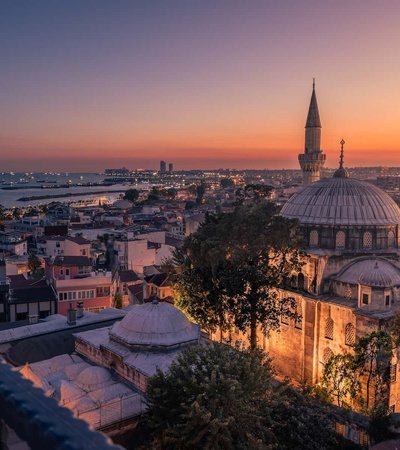 Sunset view over a historic cityscape with a mosque and the sea in the background.