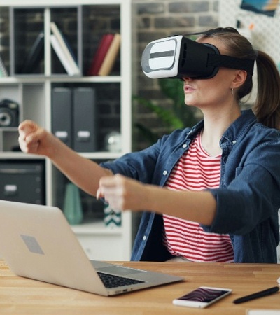 A woman is using a virtual reality headset in a home office setup, interacting with what appears to be a virtual interface.