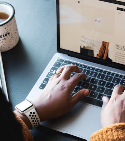 A person typing on a laptop with a cup of coffee nearby.