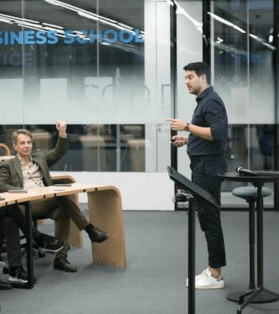 A man is presenting to a group of attentive people in a modern business school setting.