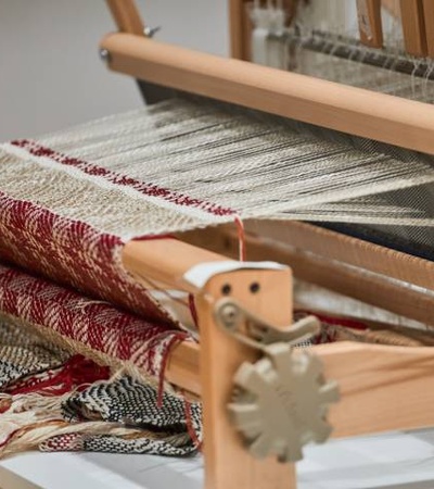 A close-up view of a wooden loom weaving red and white fabric.