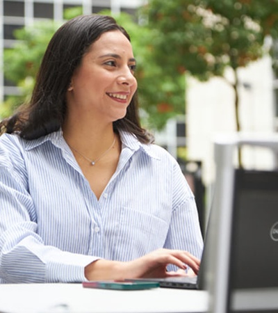 A woman smiling while working on her laptop outdoors.
