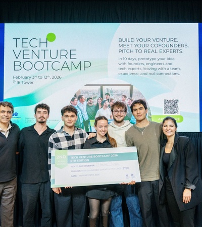A group of participants presenting their project at the Tech Venture Bootcamp in front of a promotional banner.