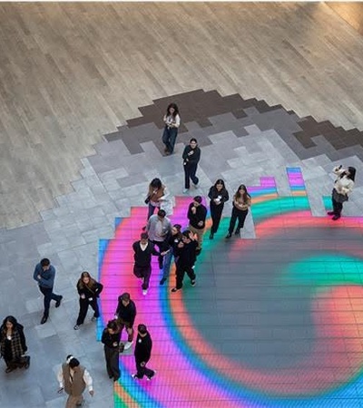 A vibrant digital art installation on the floor with people gathered around it.