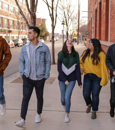 A group of five young adults walking and talking on a city sidewalk next to a brick building.