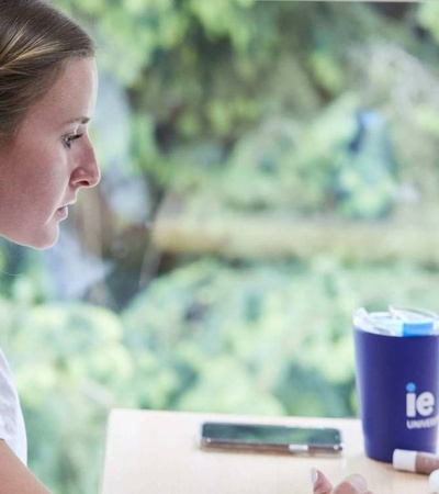 A woman wearing headphones is working on her laptop at a desk near a window.