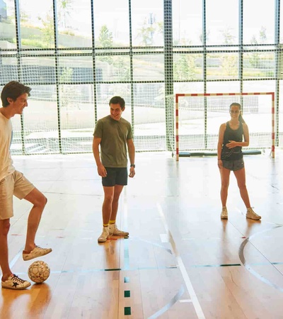 Four young adults are standing in an indoor sports court, preparing to play soccer.