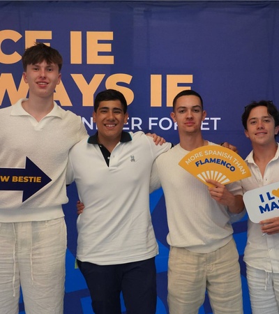 A group of four young men posing together with cheerful expressions and signs at an event.