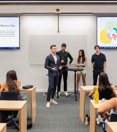 A group of students presents a business idea in a modern classroom while others listen.