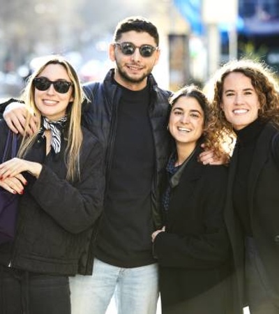 A group of four friends posing for a photo on a sunny day in the city.