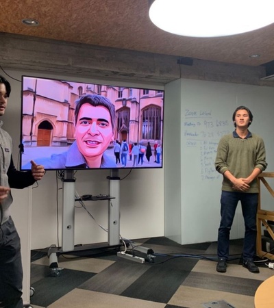 A presentation in a modern workspace featuring a speaker and a large screen with a cartoonish illustration.