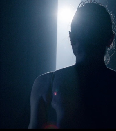 A silhouette of a person standing in front of a bright light in a dark room.