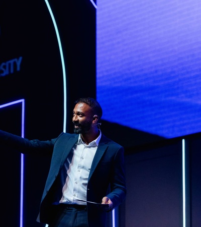 A man presenting on stage at an event with IE University branding in the background.