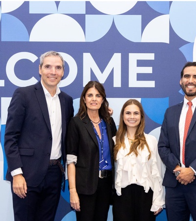 Five professionals standing in front of a blue 'IE University' welcome banner.