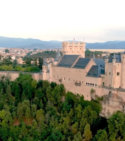 A stunning aerial view of a medieval castle surrounded by greenery with mountains in the background.