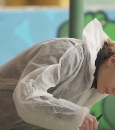 A woman in a white protective suit is painting a colorful mural on a wall.