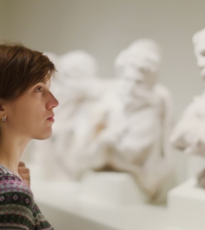 A woman gazes thoughtfully at a group of white marble sculptures in a gallery.