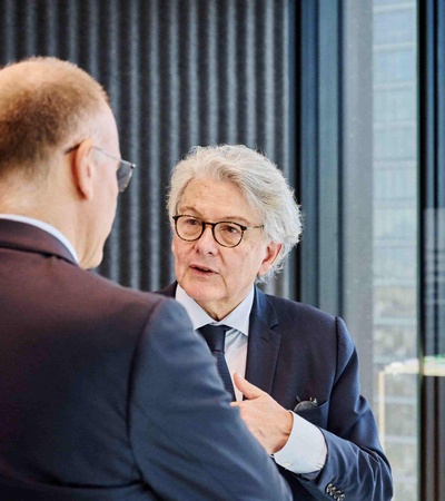 Two men are engaged in a conversation in an office setting with a modern backdrop.